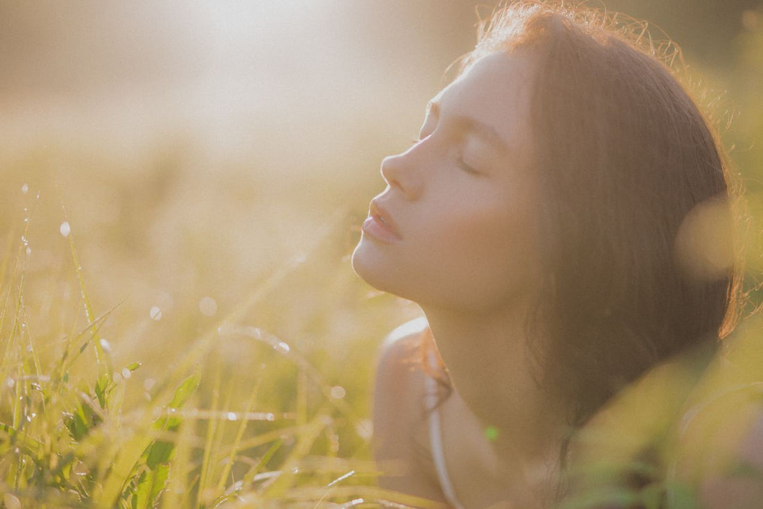 Mujer relajada con los ojos cerrados bajo la luz del sol de otoño en la naturaleza, evocando el cuidado y la calma de la piel.