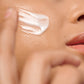 Primer plano de la textura ligera de la crema facial La Crème Repulp de Novexpert aplicándose sobre la mejilla de una mujer.