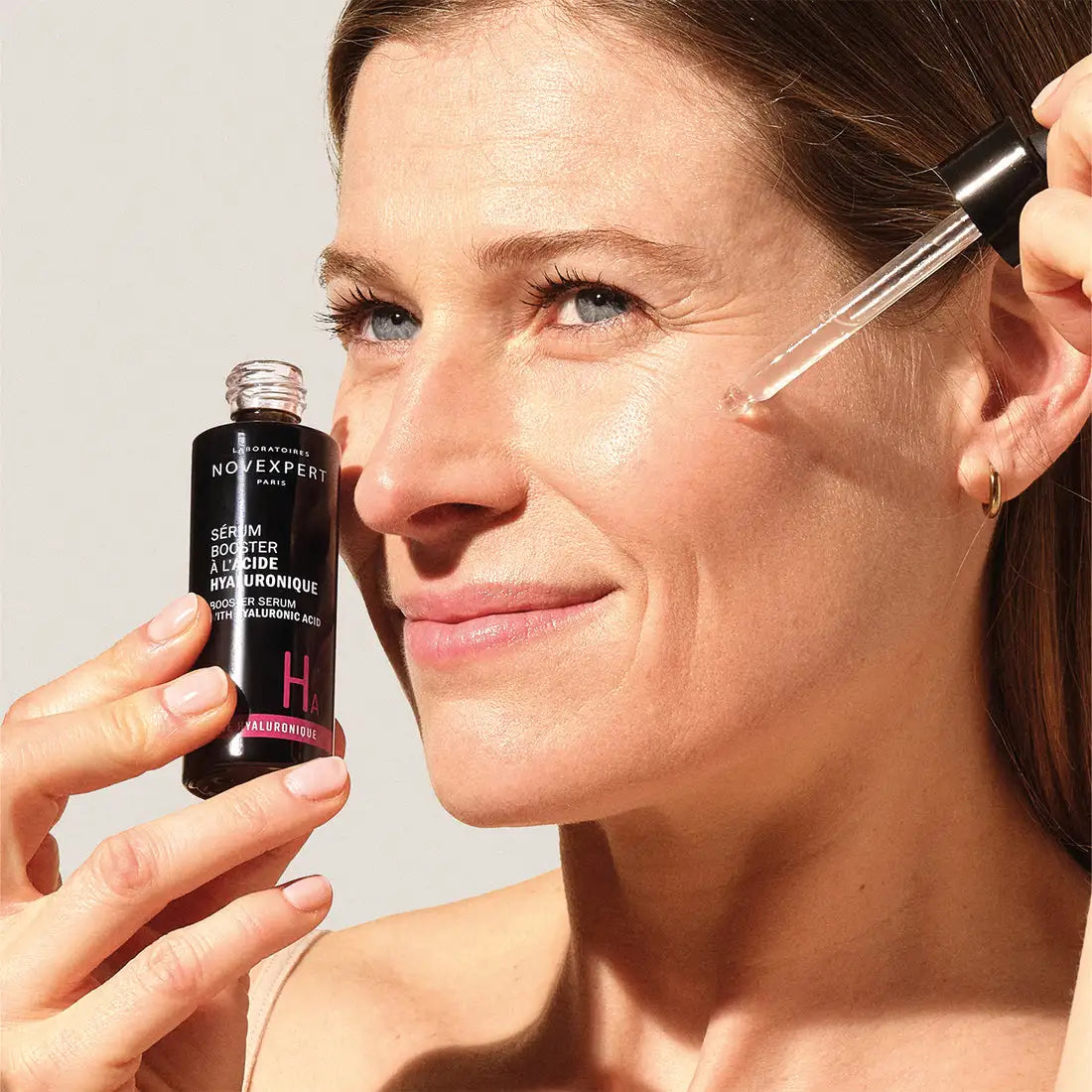  Mujer sonriente aplicando gotas del Sérum Booster con Ácido Hialurónico de Novexpert directamente en su mejilla con el gotero.