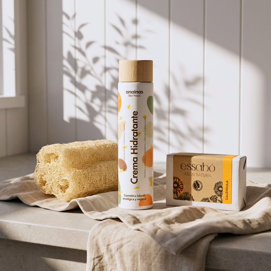 Pack de cosmética natural compuesto por Crema Hidratante Anainas, jabón artesanal de caléndula Essabó y esponja de luffa orgánica Iberluffa, dispuestos sobre una encimera de baño con iluminación suave.