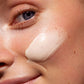 Primer plano de la textura cremosa y ligera de la crema con Vitamina C de MÁDARA aplicada sobre la mejilla de una mujer, mostrando un acabado jugoso e iluminado.
