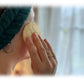 Mujer utilizando un disco exfoliante de luffa natural de Iberluffa sobre la mejilla para limpieza y exfoliación facial.