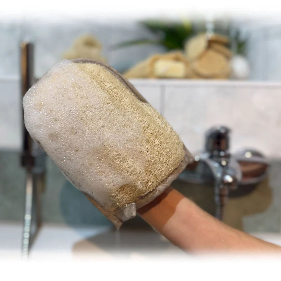 Mano utilizando la manopla de luffa natural de Iberluffa con espuma de jabón en un baño para exfoliación corporal.